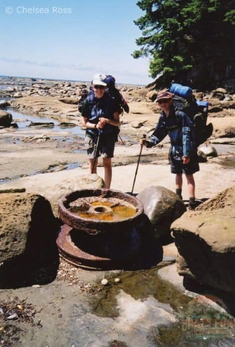 Boy and girl by an old rusted wheel on the beach