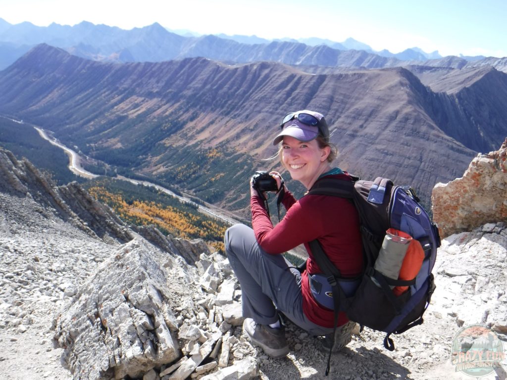 I'm crouched down on my shoes turned back with my backpack on me and camera in my hands with a mountain scenery behind me