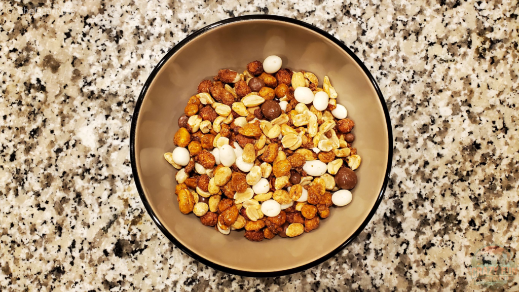 Peanut Galore Mix with nuts covered in white yogourt and chocolate in a tan bowl on a marble countertop.
