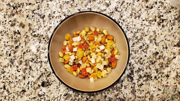 Caribbean Fruit and Nut Mix containing peanuts, almonds, dried pineapple, papaya, coconut and pumpkin seeds in a tan bowl on a countertop. They are easy snack ideas for kayaking.