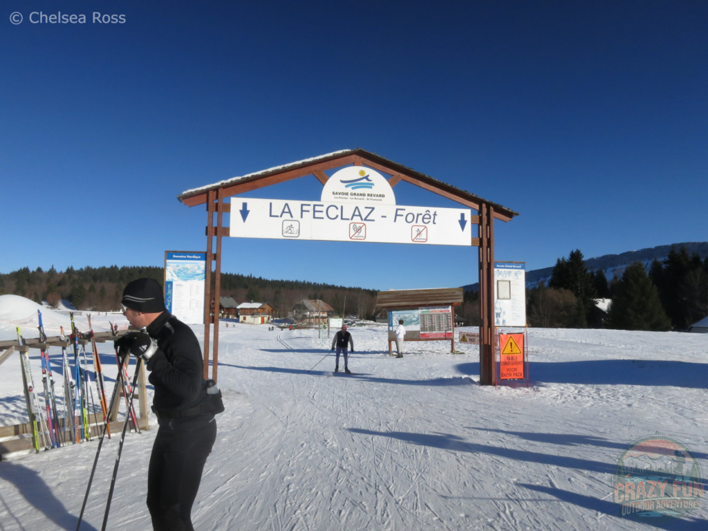 Main gate giving access to cross-country skiing La Féclaz. The ground is packed with snow with a skier exiting the area and a man to the left in black, who just finished skiing. 