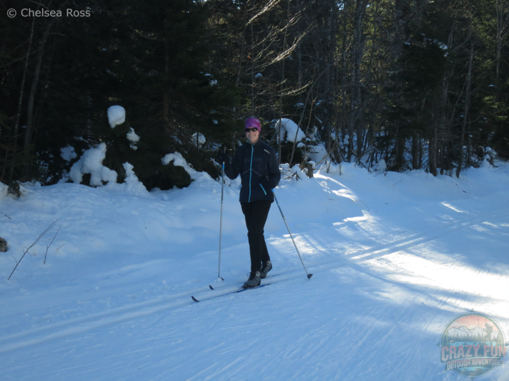 I'm cross-country skiing La Féclaz with my blue coat and black pants in the shade. Trees are seen in the background and snow covers the ground.