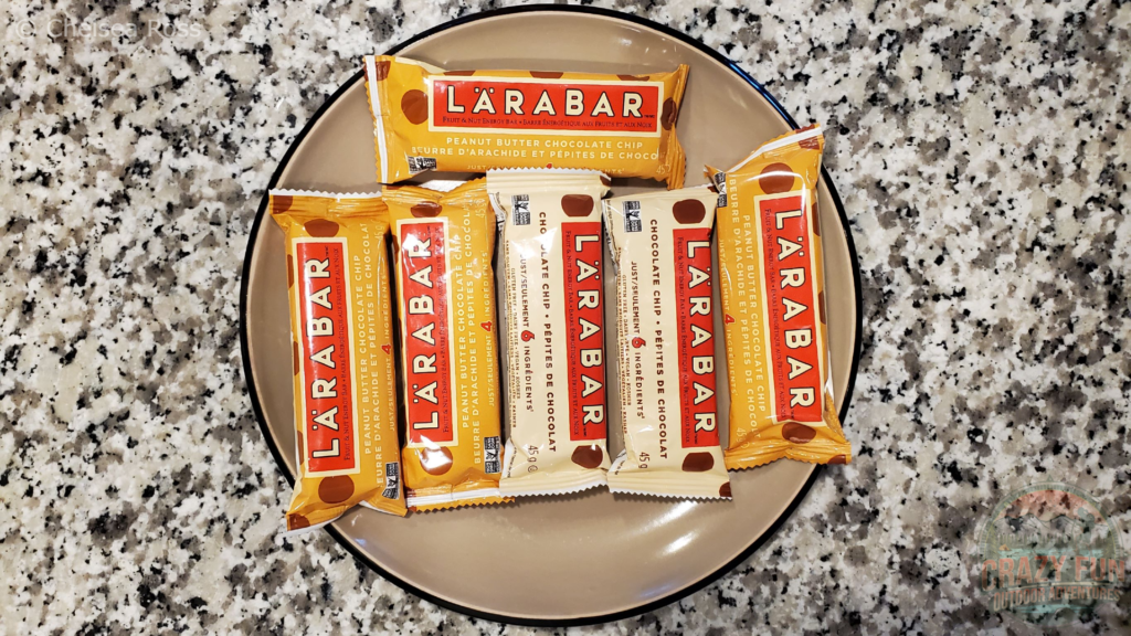 4 peanut butter Lärabars plus 2 chocolate chips Lärabars on a tan plate on a marble countertop.