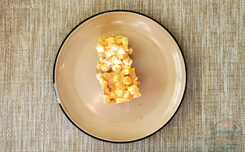 Two peanut butter marshmallow squares sit on a plate showing what they look like when finished. They have four or five layers of marshmallows with peanut butter in between.  