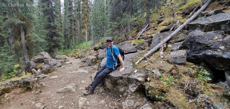 Man with blue t-shirt and backpack is taking a break as he sits on a rock hiking to Laughing Falls.