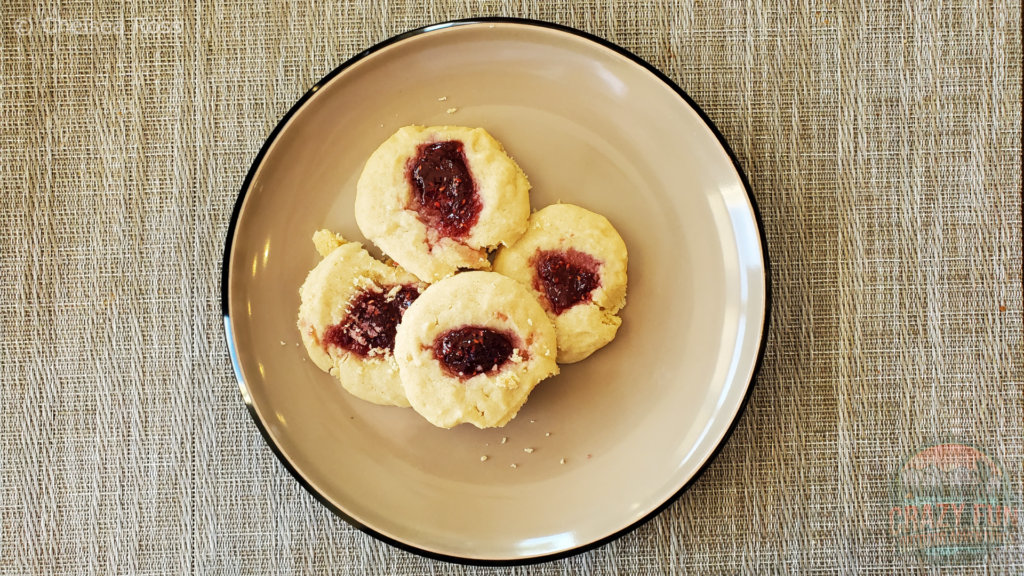 Vegan Raspberry Thumbprint (raspberry in the center of the beige cookies) sits on the plate. 