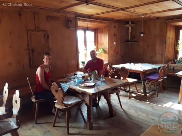 Kris and I sitting at table inside the b & b having breakfast. They offered cheese, yogourt, bread, chacuterie, boiled egg. The walls are made of wood on our unforgettable hiking holiday in Bolzano.