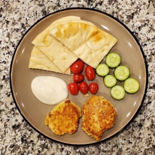 Two salmon patties are on the plate surrounded by tomatoes and cucumbers.