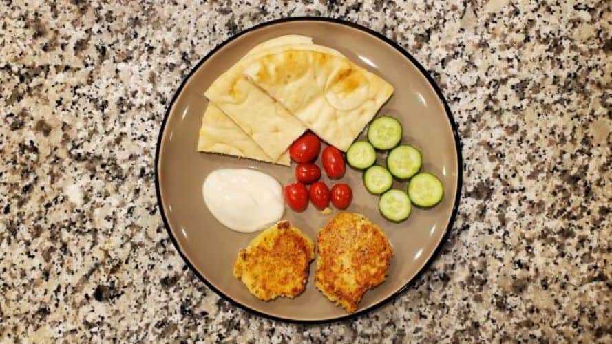 Two salmon patties are on the plate surrounded by tomatoes and cucumbers.