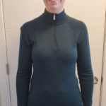 I'm standing in front of a white door while wearing my green Merino 250 Top Base Layer ready for cross-country skiing.