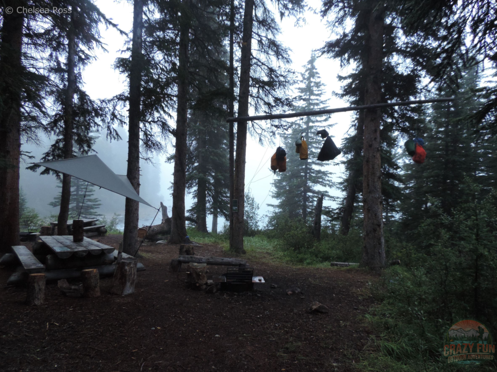 Looking at the cooking area, protected by a tarp in case it's starts raining on us again. The bear cache is to the right with the food in bags hanging up in the trees. It's very foggy in the background. 