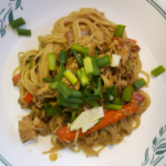 Thai Chicken Pasta meal on a white plate on the counter that includes pasta, chicken, carrot, green onions and napa cabbage. It's a delicious meal after a day of hiking.