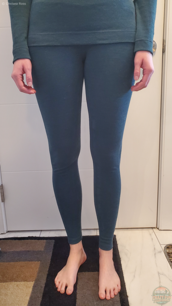 Picture showing me wearing the Merino pant base layer for women. A white door is behind me along with a black, grey, and brown rug underneath my bare feet.
