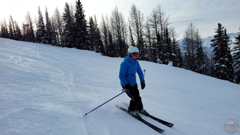 Lady heading down the blue larch run in a blue jacket and navy pants while kicking up snow downhill skiing.