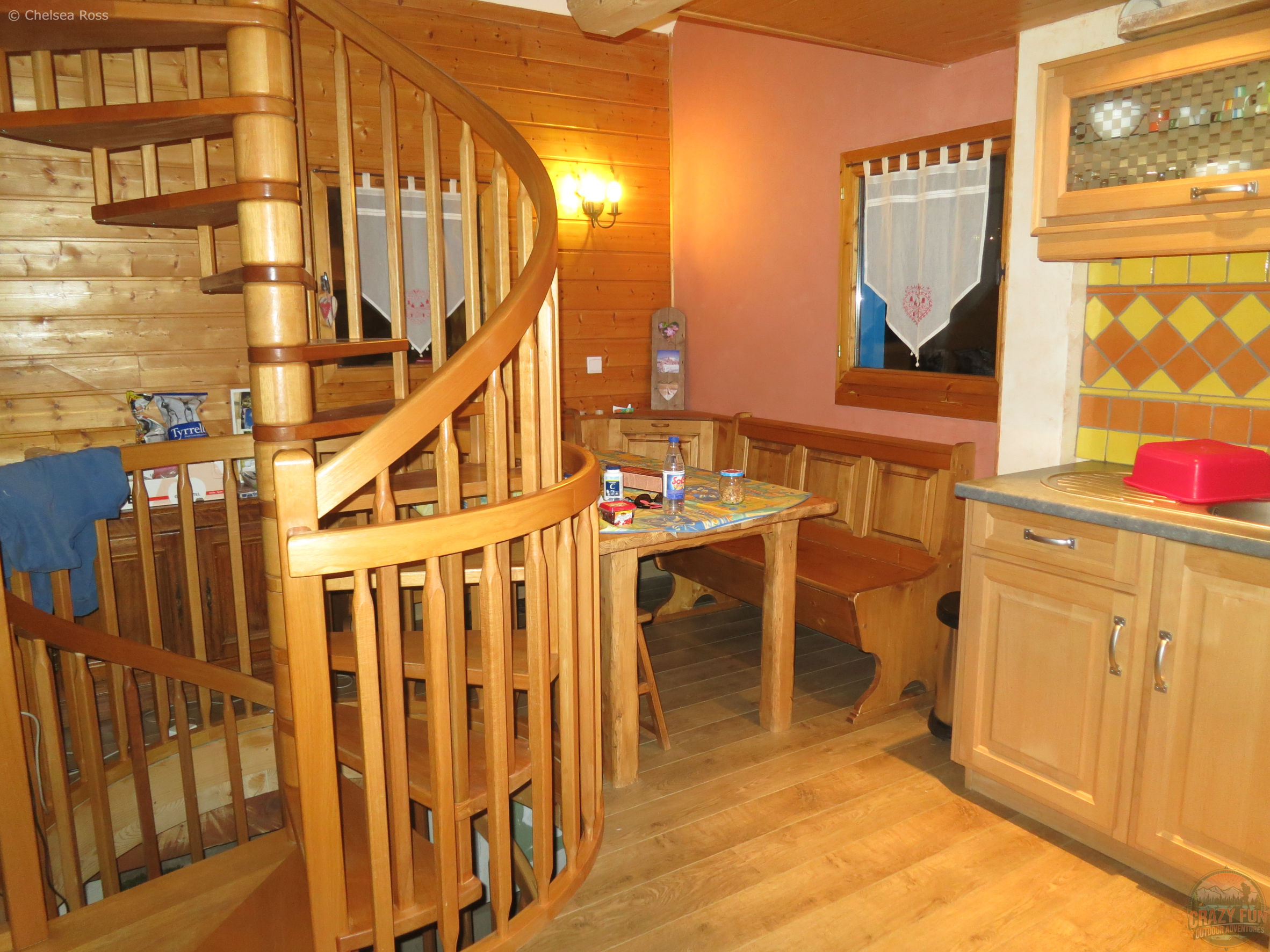 The inside of the chalet showcasing the main floor. It has circular wooden stairs, a sitting area in the corner with a kitchen to the far right.