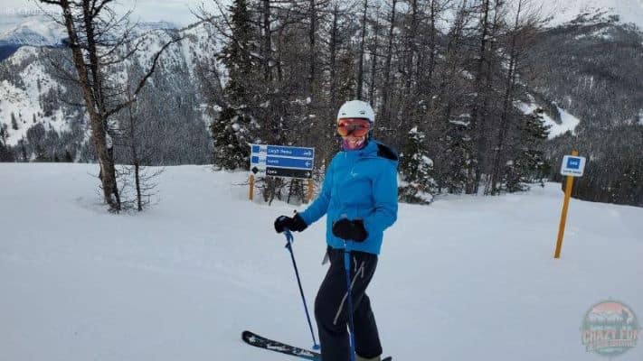 Lady standing in front of a directional sign with a blue coat and navy pants on skis. 