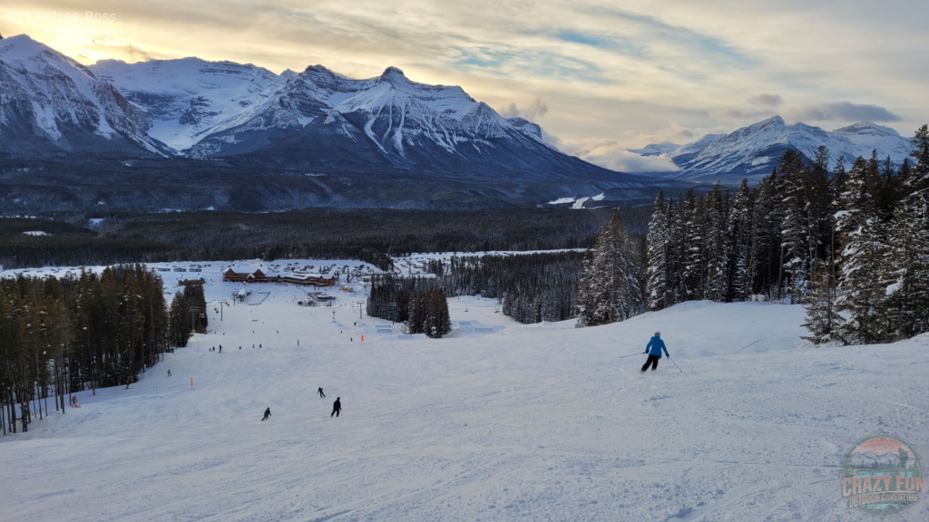 Downhill ski Sunshine or Lake Louise? I'm heading down to the bottom of the Lake Louise ski hill at the end of an awesome day! Mountains can be seen across the skyline with trees all around me.