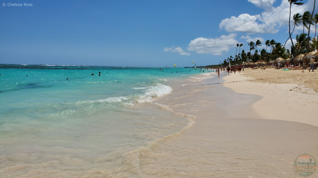 Top 10 Activities from Majestic Resorts: kayaking is number 3. A picture showing the beach on the right and the ocean on the left. People are walking on the beach with palm trees and clouds are to the far right. 
