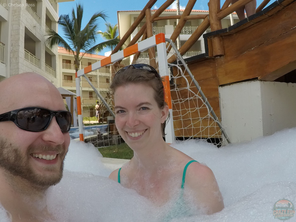 Top 10 Activities from Majestic Resorts: foam pool party is last. Kris to the left is wearing sunglasses and I'm to his right. Bubbles are surrounding us. 