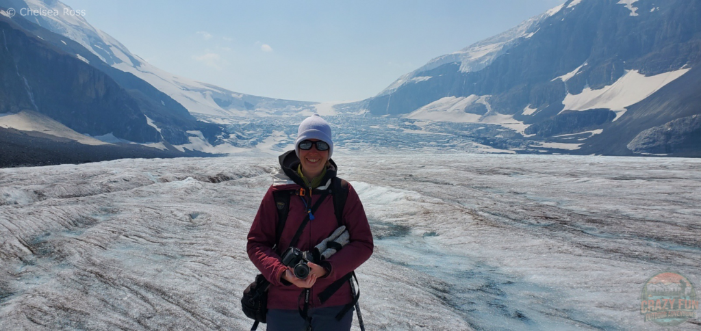 Gorgeous Athabasca Glacier Hike: I'm standing in my purple jacket with my backpack on holding my camera in my hands. The glacier can be seen in the background.