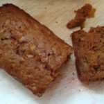 The carrot apple loaf is on a white cutting board. There's the big piece of loaf to the left and a cut piece to see the inside to the right.