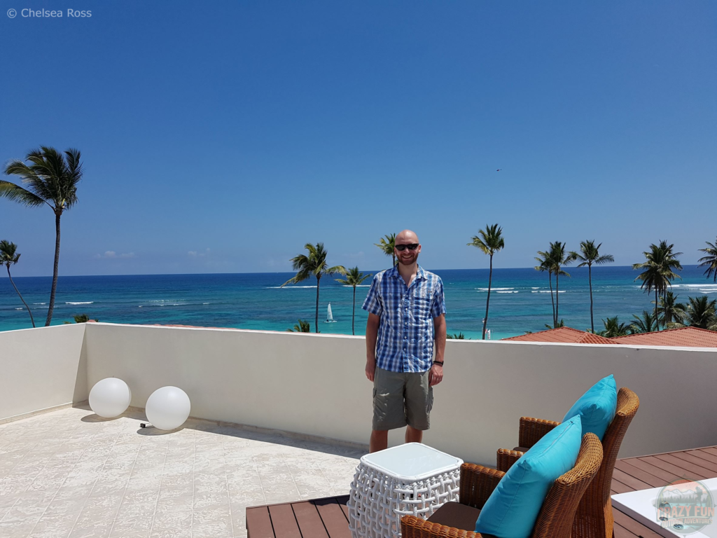 Showing Kris on our balcony with the ocean and palm trees behind him. He's wearing a casual shirt that causes discomfort when you have a sunburn. 