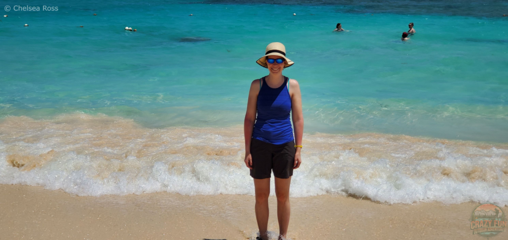 10 Tips to Avoid Sunburn: a large hat to cover your shoulders from the sun. I'm wearing a large sun hat with a blue tank top and black shorts while standing in front of the ocean. 