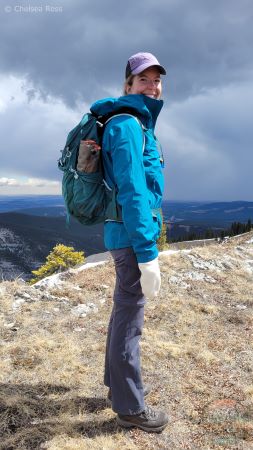 Lady in a blue coat standing at the top of Prairie Mountain. The seat cushion is in a side pocket.