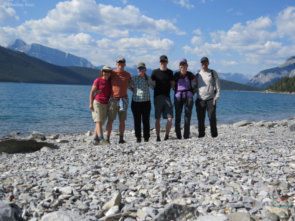 My family and I have a love for the outdoors. We are taking a picture in front of Lake Minnewanka with mountains behind us while hiking. 