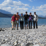 My family and I have a love for the outdoors. We are taking a picture in front of Lake Minnewanka with mountains behind us while hiking.