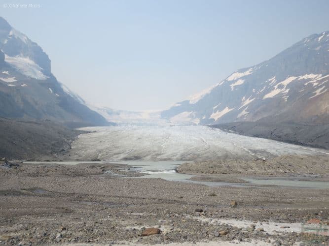 Athabasca Glacier Hike: looking at the foot of the glacier with sand at the bottom and the ice further up. Mountains can be seen on both sides. 