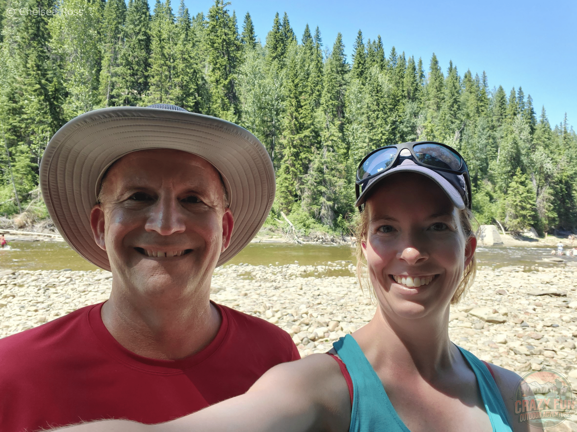 Edmonton Day Trips: Fred in red shirt and I in turquoise tank top taking a selfie in front of Pembina River with trees in the background.