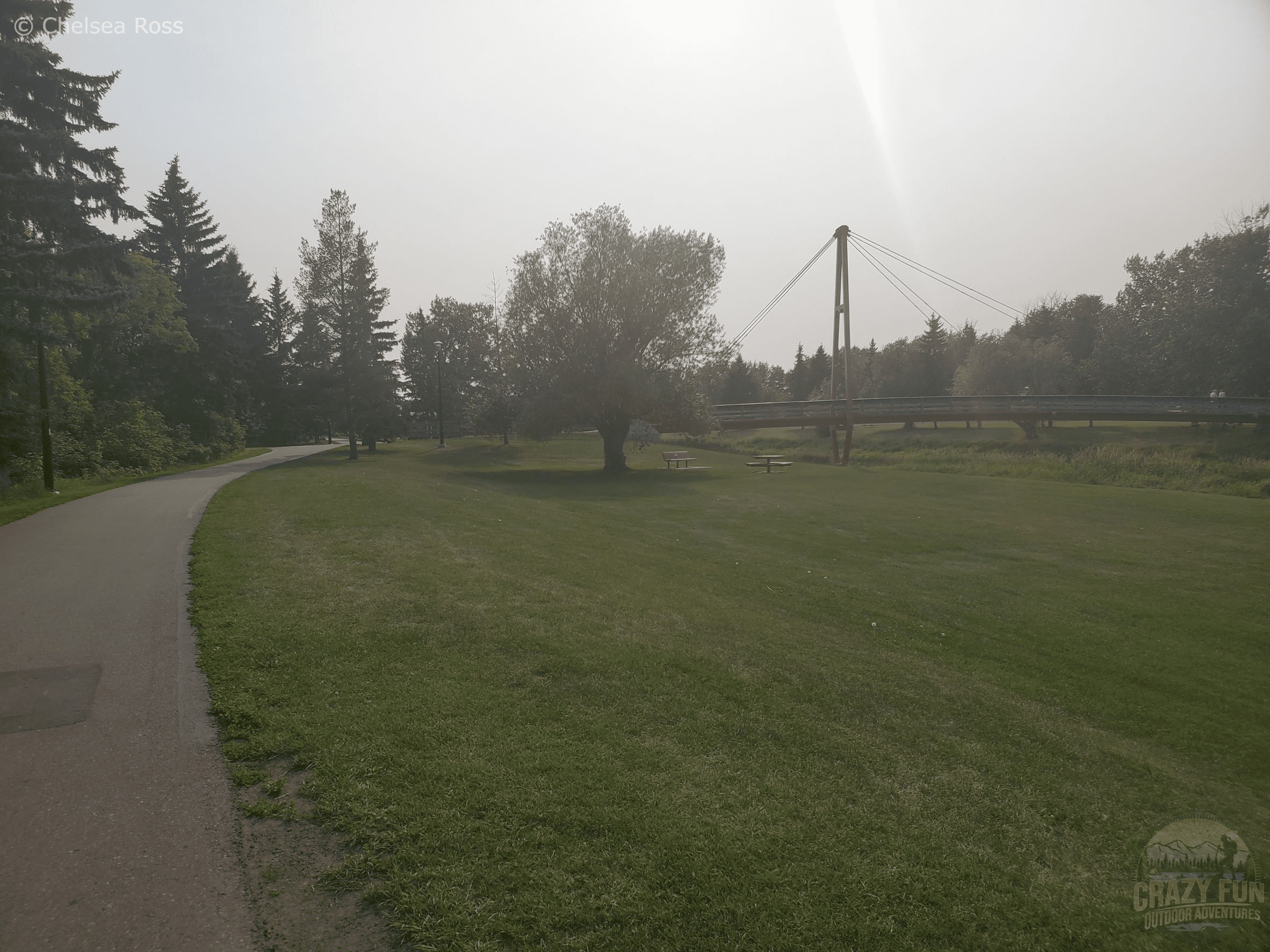 A bridge joining the north and south pathways. A green grassy field is to the right with the path to the left.