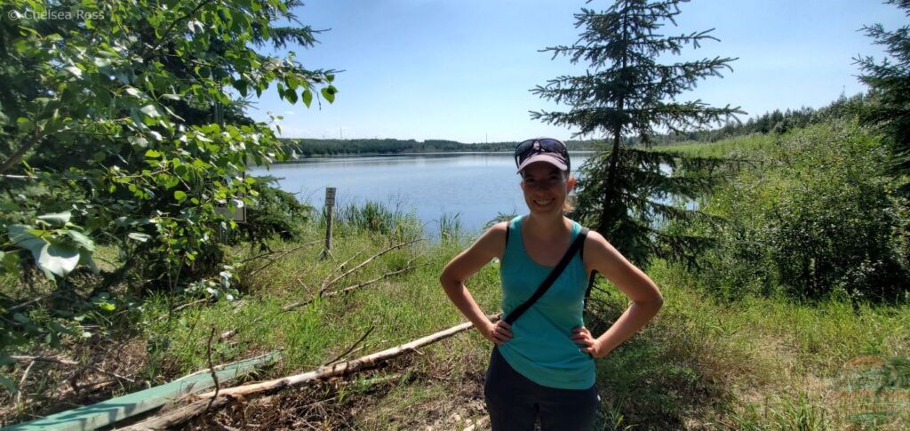 Lady standing in front of Crane Lake wearing a turquoise tank top with a purple hat and sunglasses.
