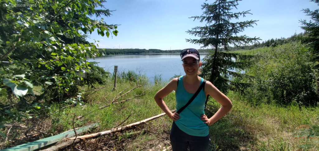 Kris took a picture of me standing in front of Crane Lake. I'm wearing a turquoise tank top with a purple hat and sunglasses.