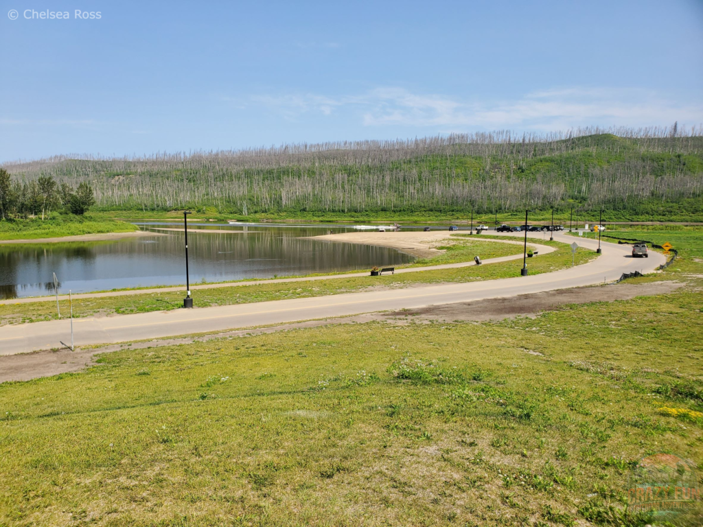 A paved path that curves in the middle with grass on either side and Clearwater River in the back.