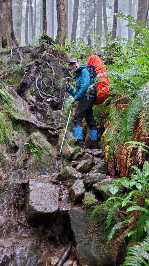 I'm standing on rocks on the WCT with my blue raincoat, black rain pants, and blue and black gaiters while wearing a backpack. Our WCT packing list will help to pack for a wonderful backpacking trip. 