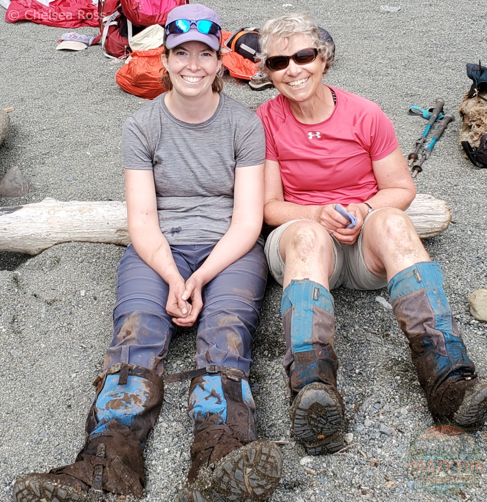 WCT packing list: boots and gaiters. My mom and I are sitting on the sand with our boots and gaiters covered in mud after a day of backpacking the WCT. 