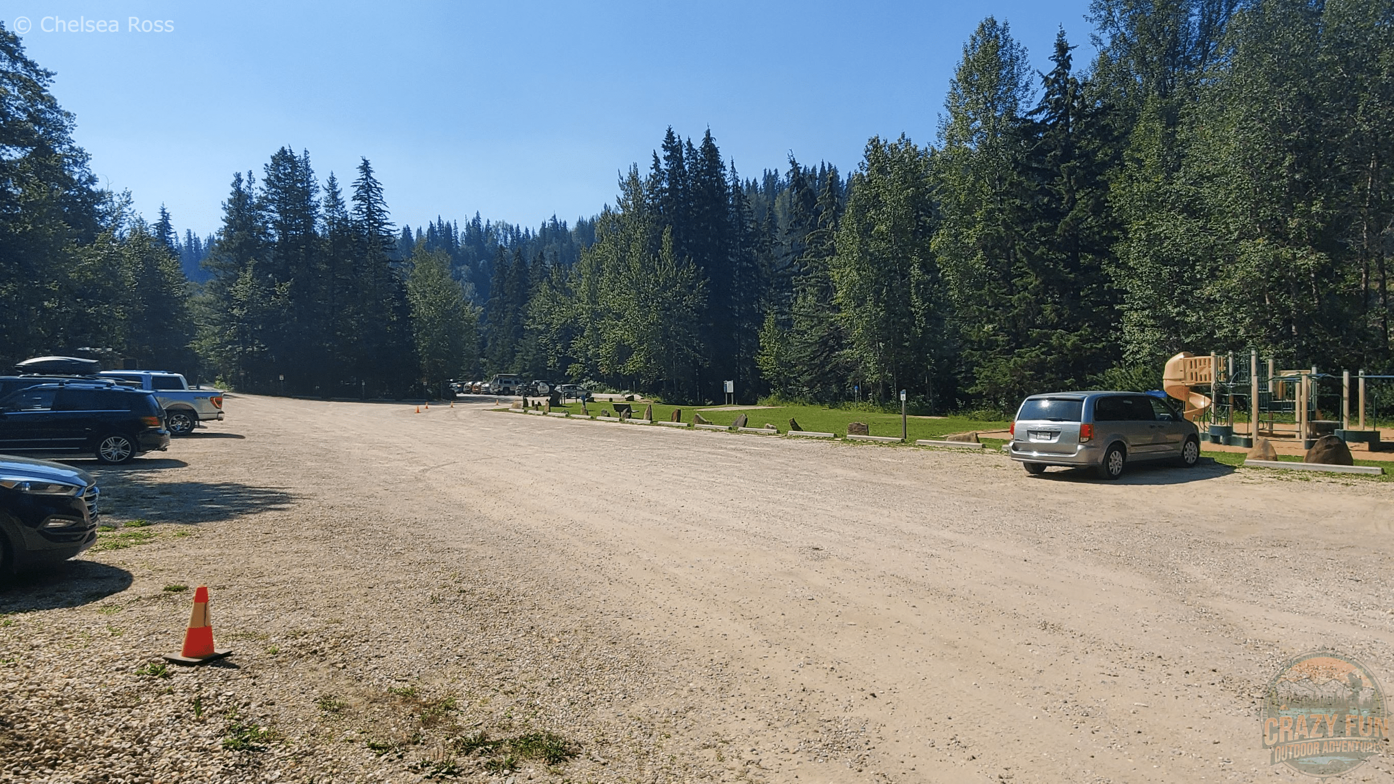 The gravel parking lot with trees surrounding it. A playground is in the right of the picture.