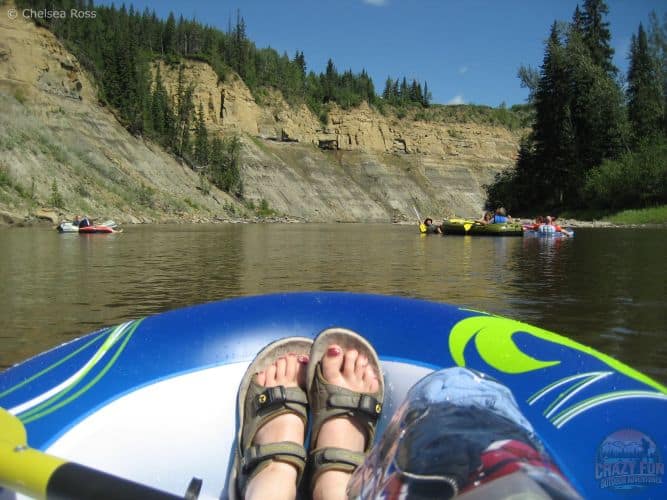 A picture of my feet in sandals in the raft with my clear bag holding my contents to keep them waterproof. Groups of rafters are in front on the calm waters.