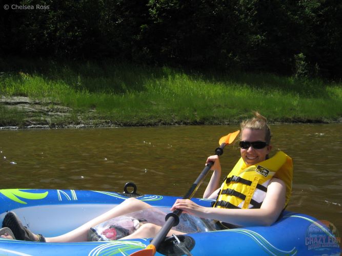 I'm having an Pembina River rafting day in the gorgeous Alberta heat. I'm sitting in my blue and white raft by myself on the water with my yellow lifejacket while holding my paddle with my clear bag between my legs.