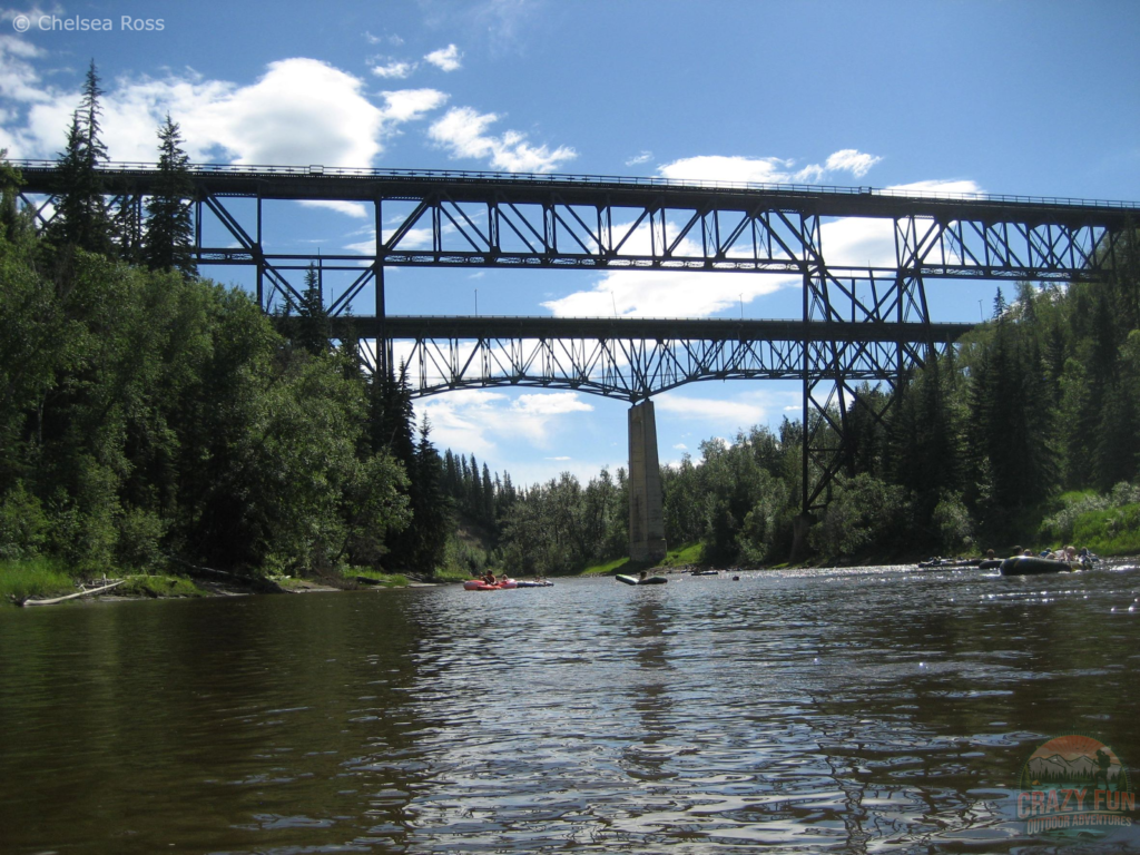 Two bridges are seen in front that we are about to go under on our Pembina River rafting day. Different groups of rafters are in front. 