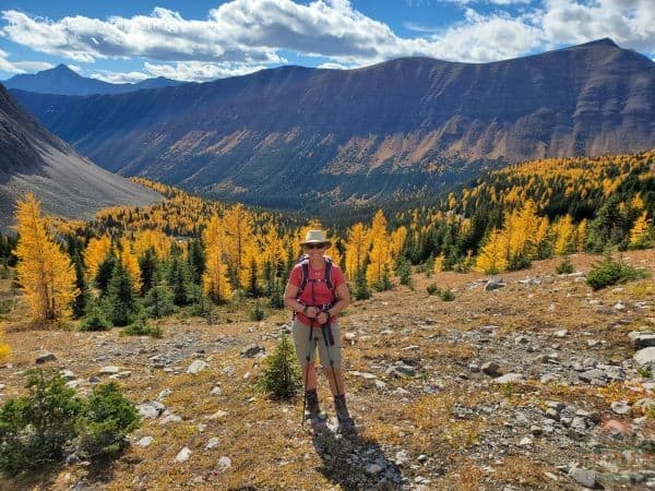 The best larch hikes showcasing lady at Little Arethusa with beautiful larches and a mountain behind her.