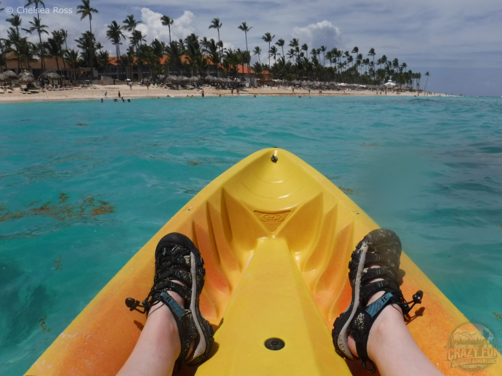 The tip of the yellow kayak we are sitting in with my sandals showing and the beach far ahead.