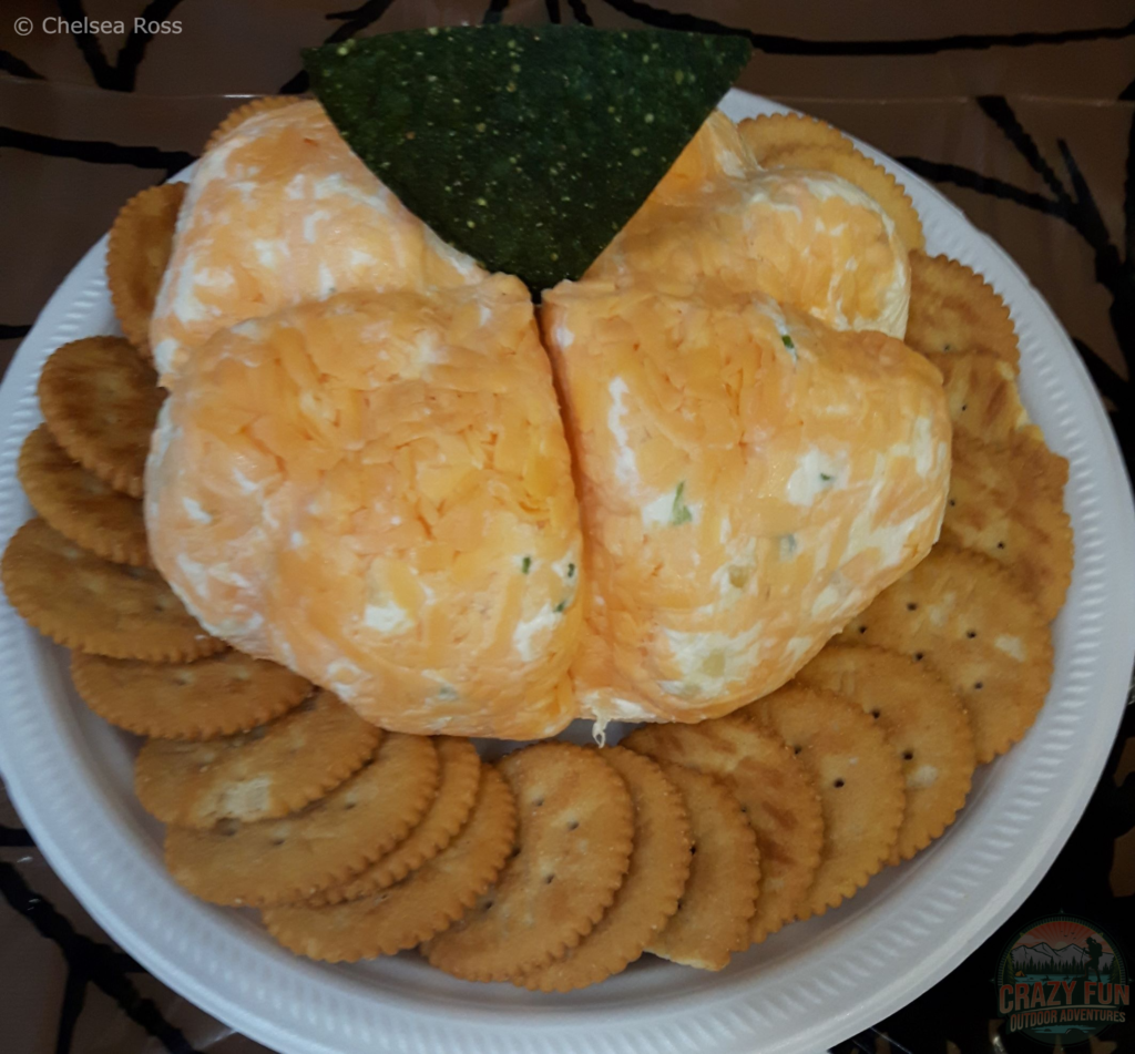Halloween Party Treats include a pumpkin cheese ball with crackers around it and a green chip in it. 