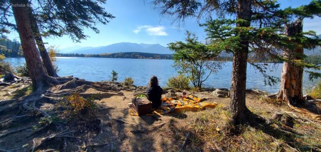 Fall Experiences Near Me shows lady sitting for a picnic with the mountains in the background.