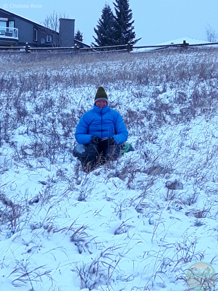 My dad sitting on a tube in the middle of the hill, he didn't go very far sledding. He's sitting in the tube with a blue jacket.