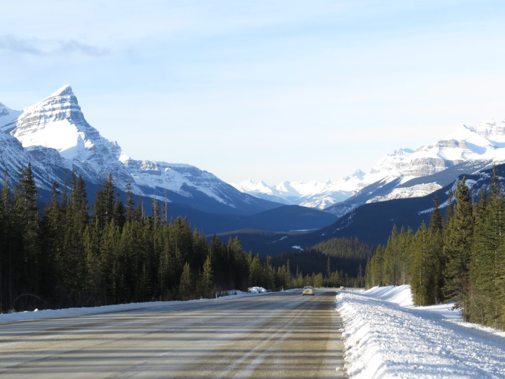 What are the benefits of skiing? A road with mountains behind making it a beautiful scenery. 