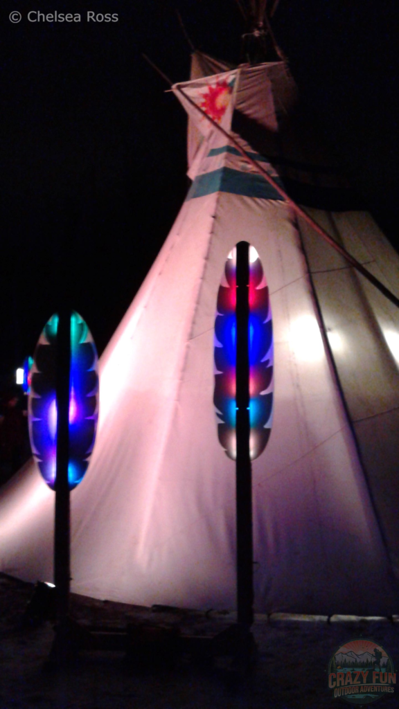 A tipi with different coloured feathers in front of it.