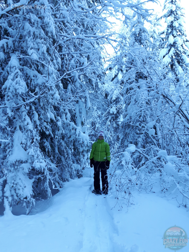 My mom is snowshoeing in between trees covered in snow.